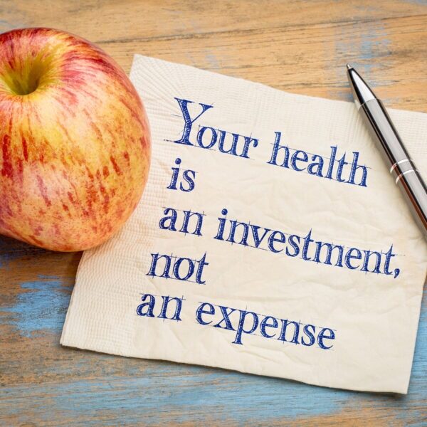 Your health is an investment, not an expense - wellness concept - handwriting on a napkin with a fresh apple